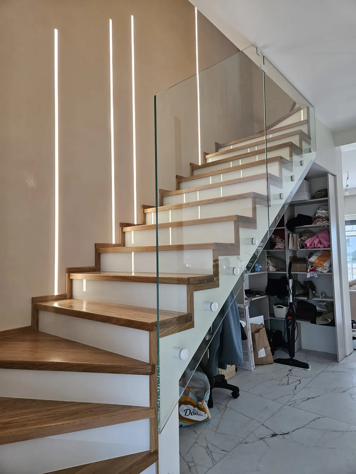 Bezramowa balustrada szklana wzdłuż schodów z drewnianymi stopniami i listwami LED